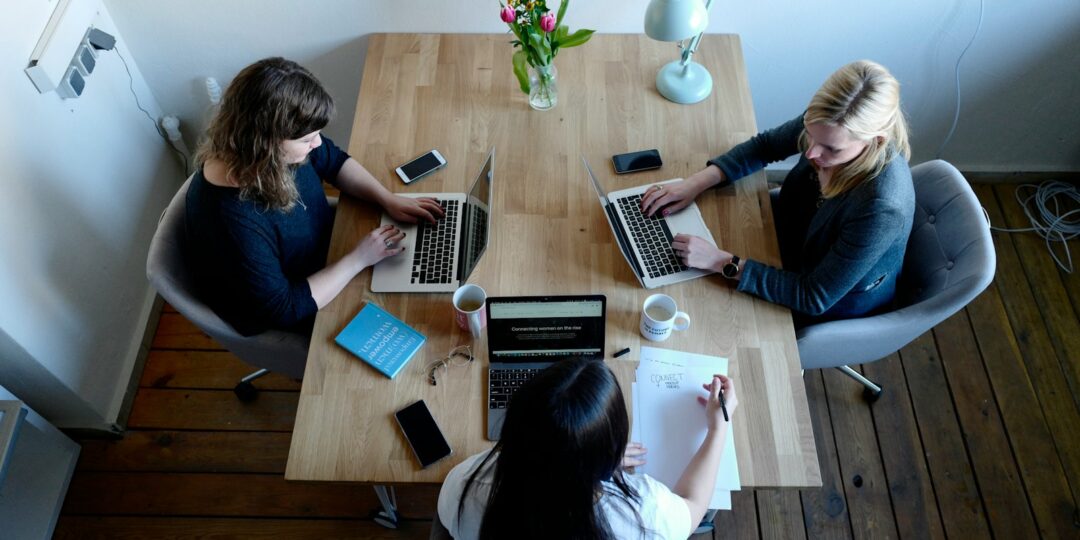 three women sitting around table using laptops