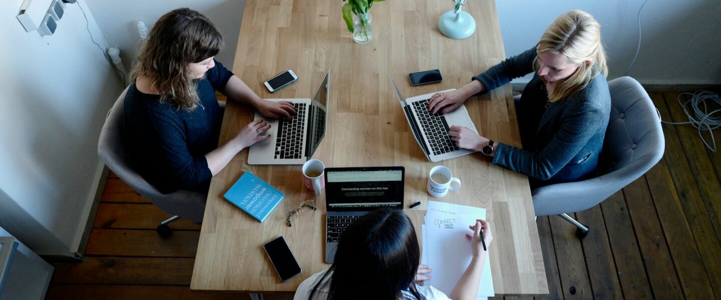 three women sitting around table using laptops